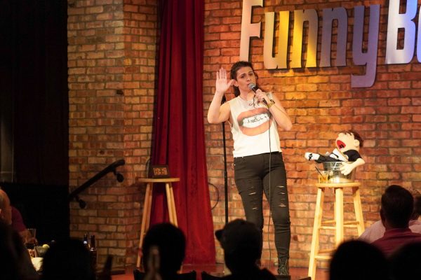 A comedian on stage with the Just Call Moe puppet in 2024