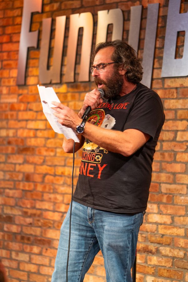 A comedian reading audience votes off a sheet of paper in 2025