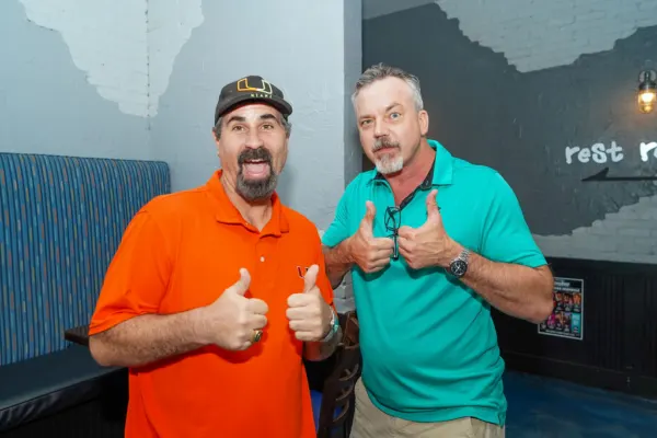Two men in orange and teal polos giving double thumbs up