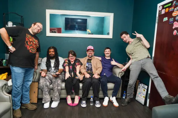 The cast posing together on a couch against a teal wall