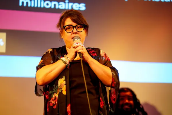 A comedian in a floral kimono performing in front of the screen