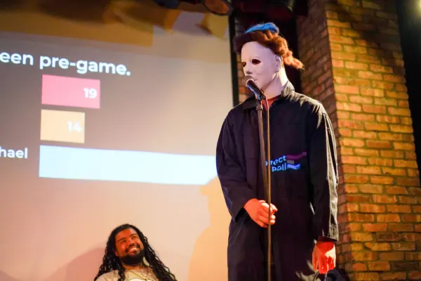 A performer in a white mask in front of the Halloween pre-game poll